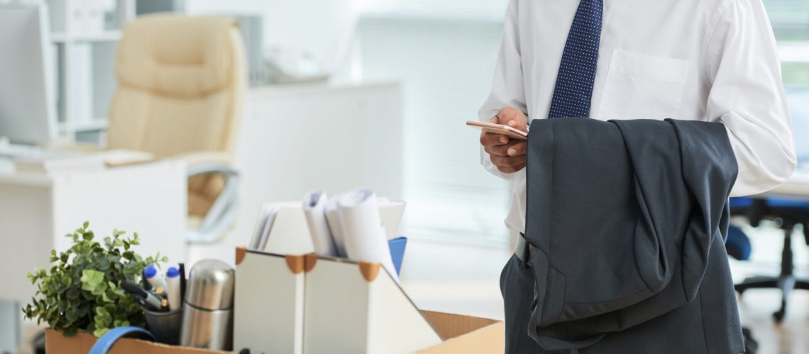 unrecognizable-man-standing-office-using-smartphone-with-personal-belongings-box